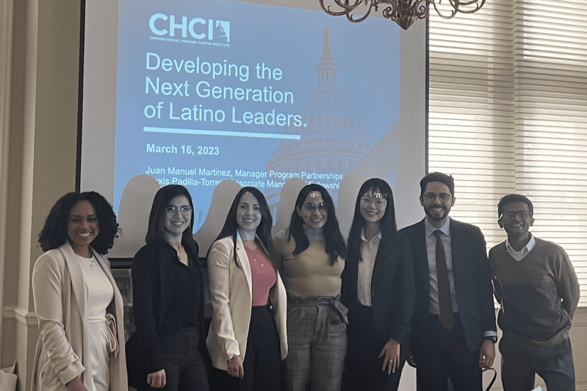 Seven students standing in front of a screen with text that reads "Developing the Next Generation of Latino Leaders."